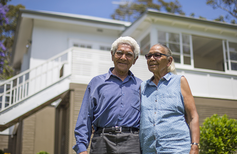 An elderly couple standing in front of a house