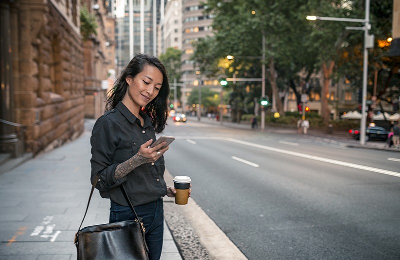 A woman wearing business casual standing on a city street and looking at her phone